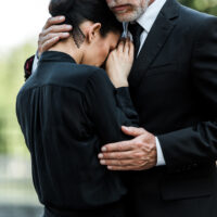 cropped view of sad elderly man embracing woman on funeral